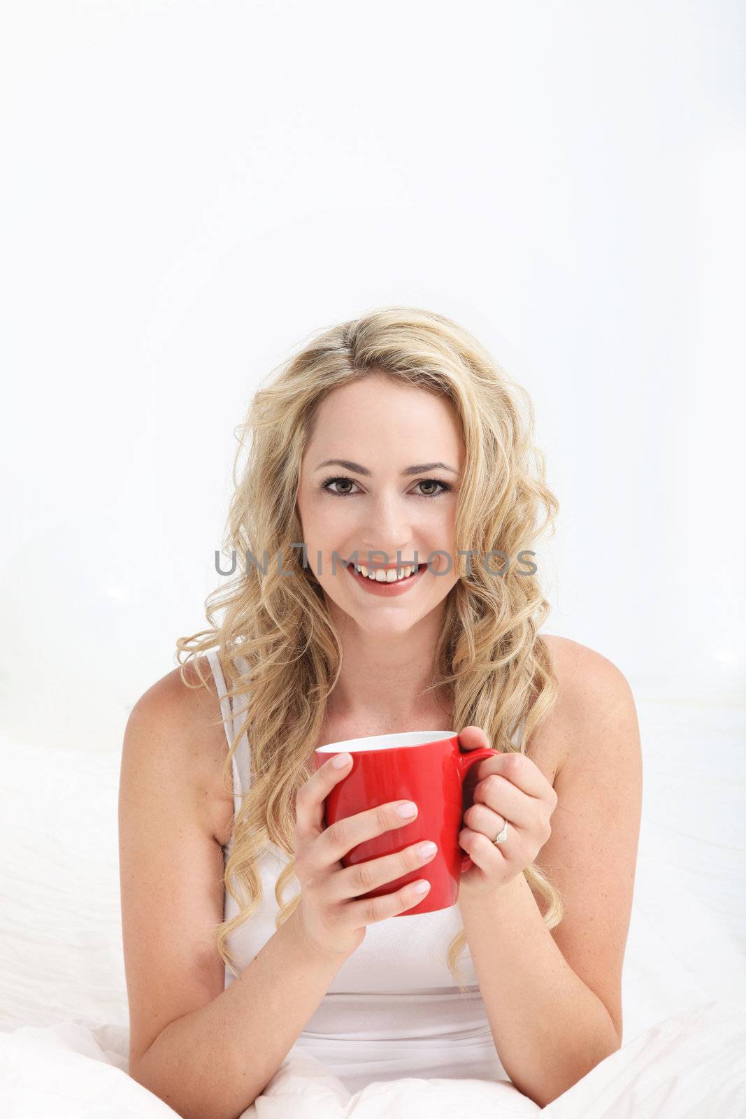 Smiling happy young woman looking refreshed after a good nights sleep enjoying a mug of coffee in bed