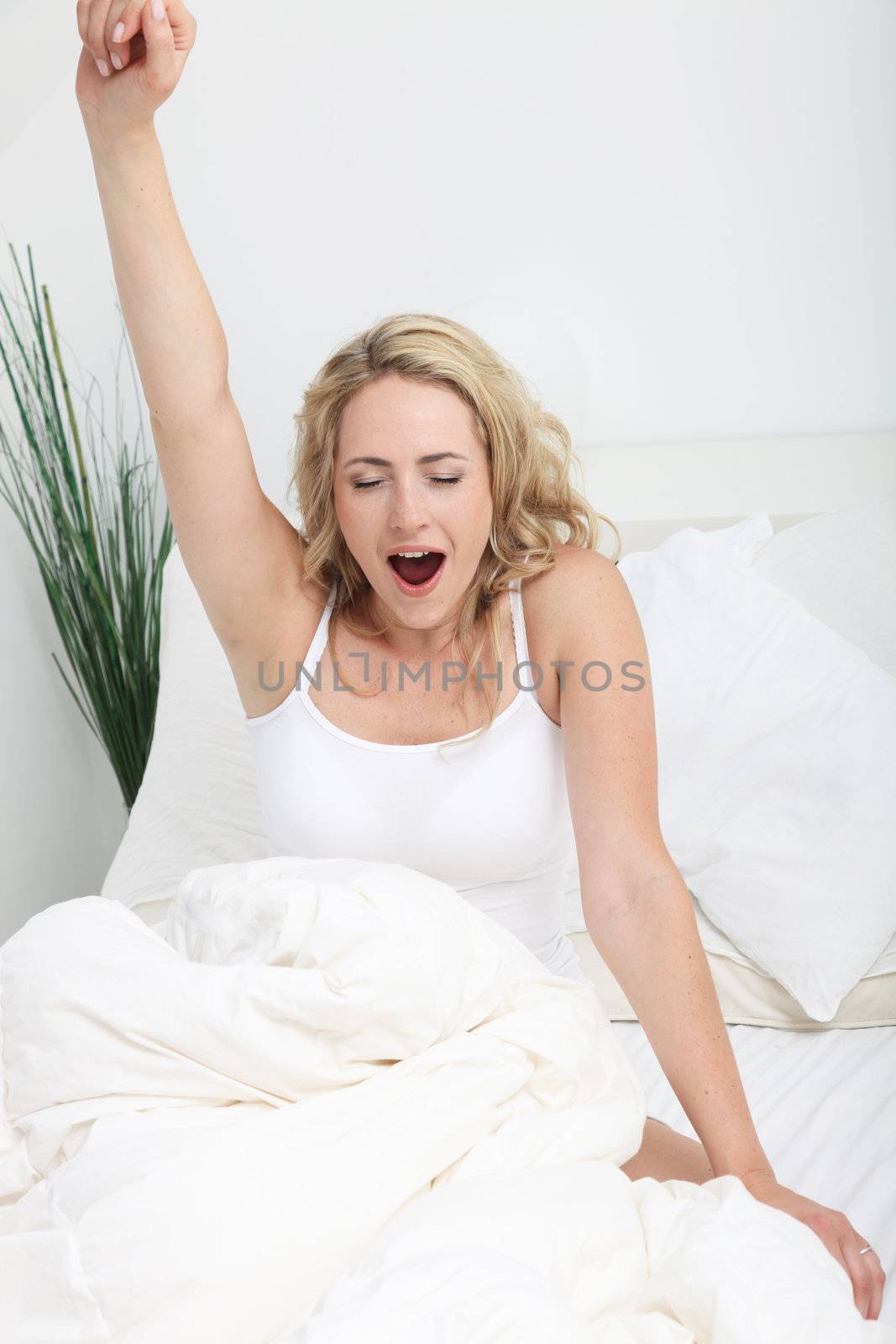 Young woman stretching and yawning in bed as she prepares to get up to start her day