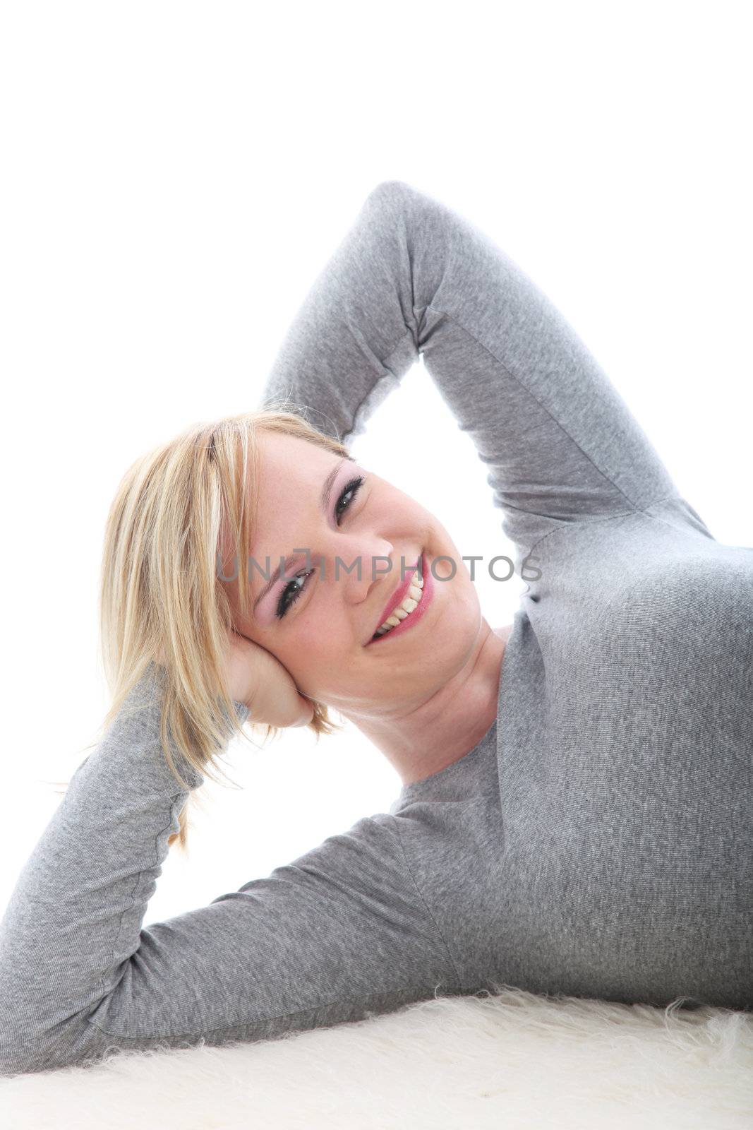 Happy woman lying on a fluffy white carpet smiling in satisfaction as she stretches her arms behind her head