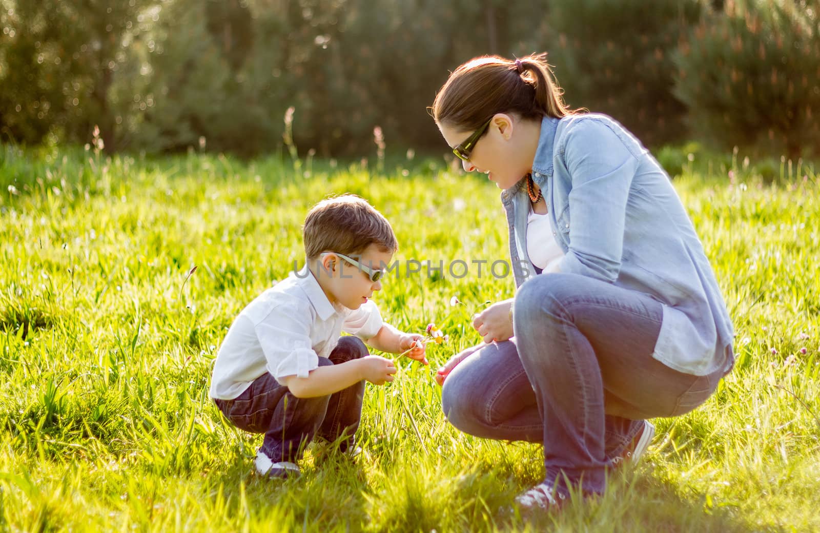 Happy mother and cute son picking a bouquet of flowers in a sunny field