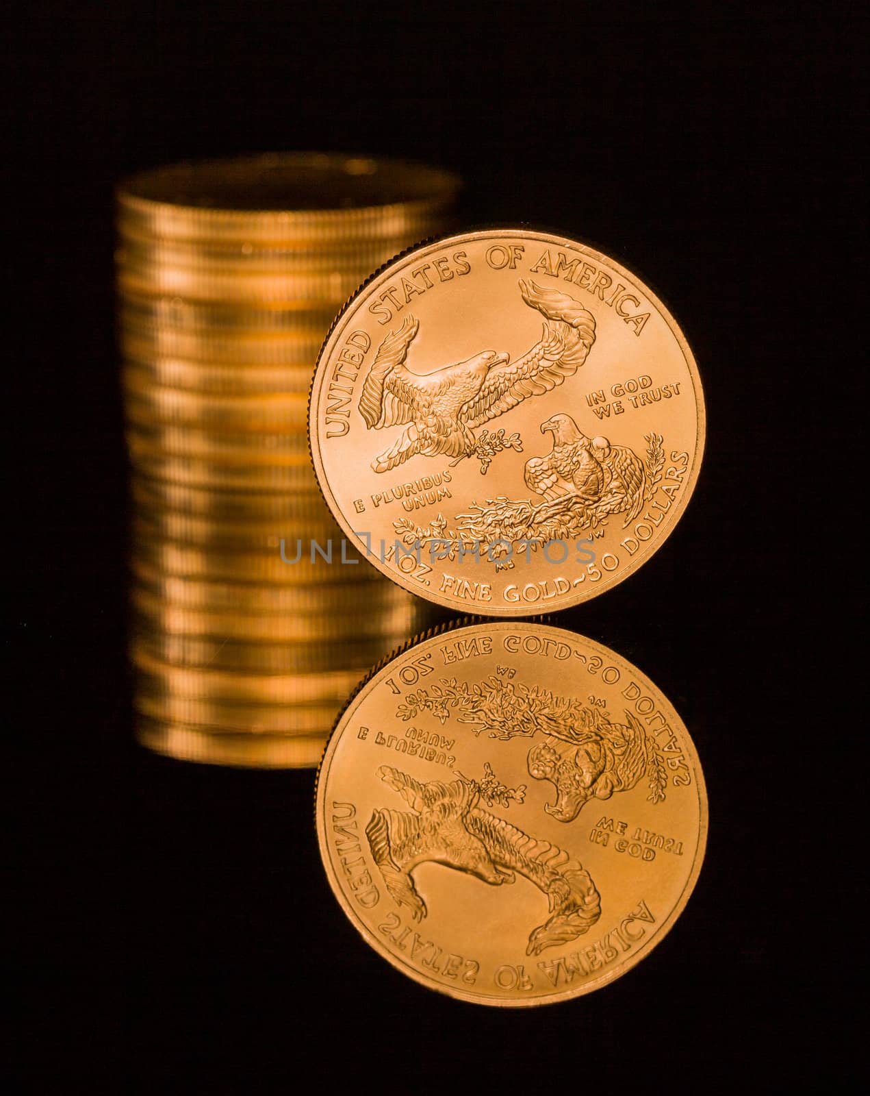 Reflection of single gold coin and stack on black polished surface