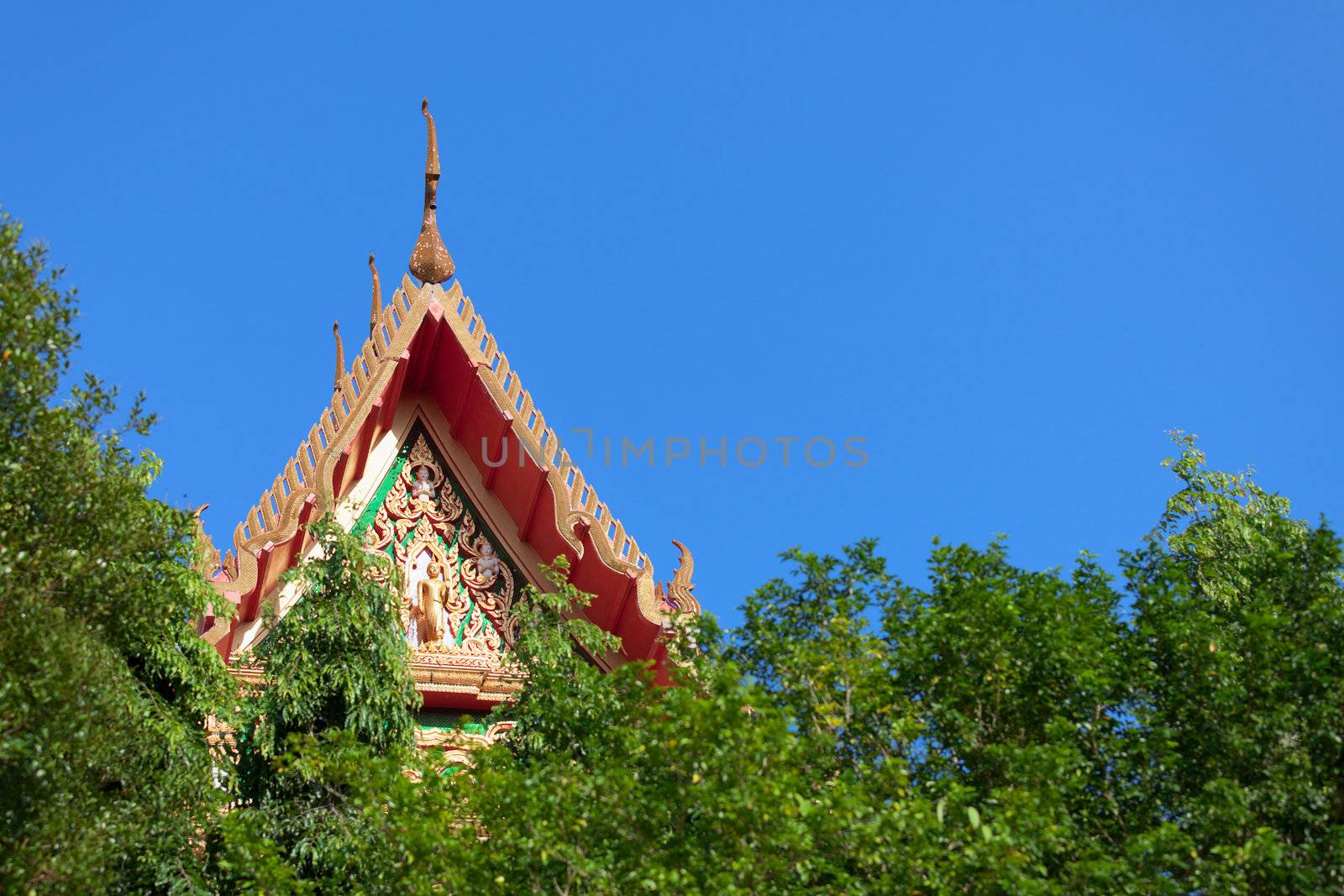 The roof of a Thai Buddhist monastery over the trees