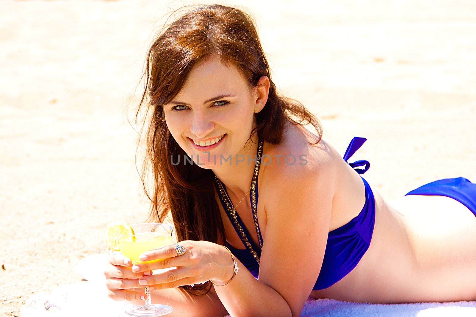 Photo of a young and beautiful woman who is resting on the beach and drink a drink from a glass