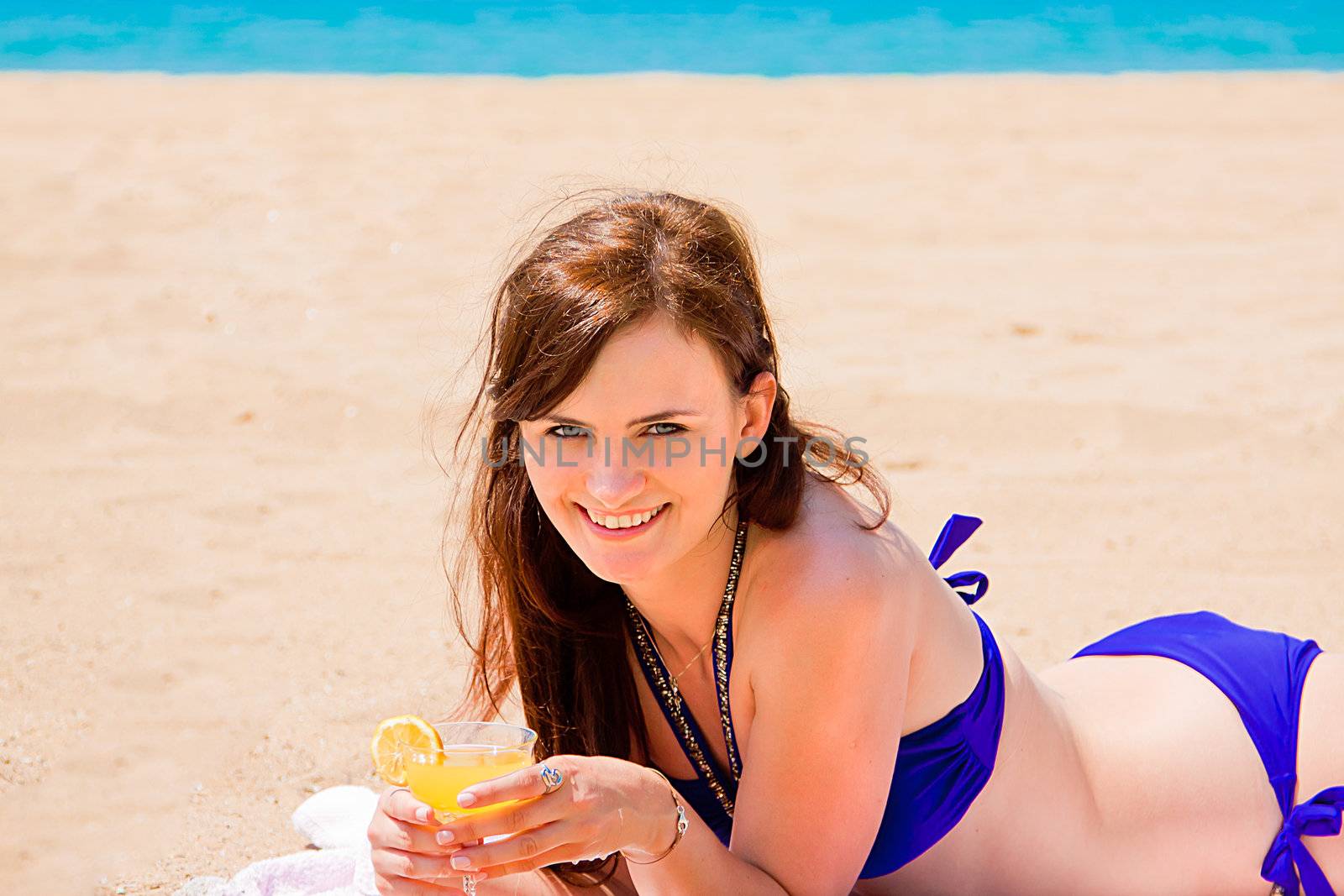 Photo of a young and beautiful woman who is resting on the beach and drink a drink from a glass