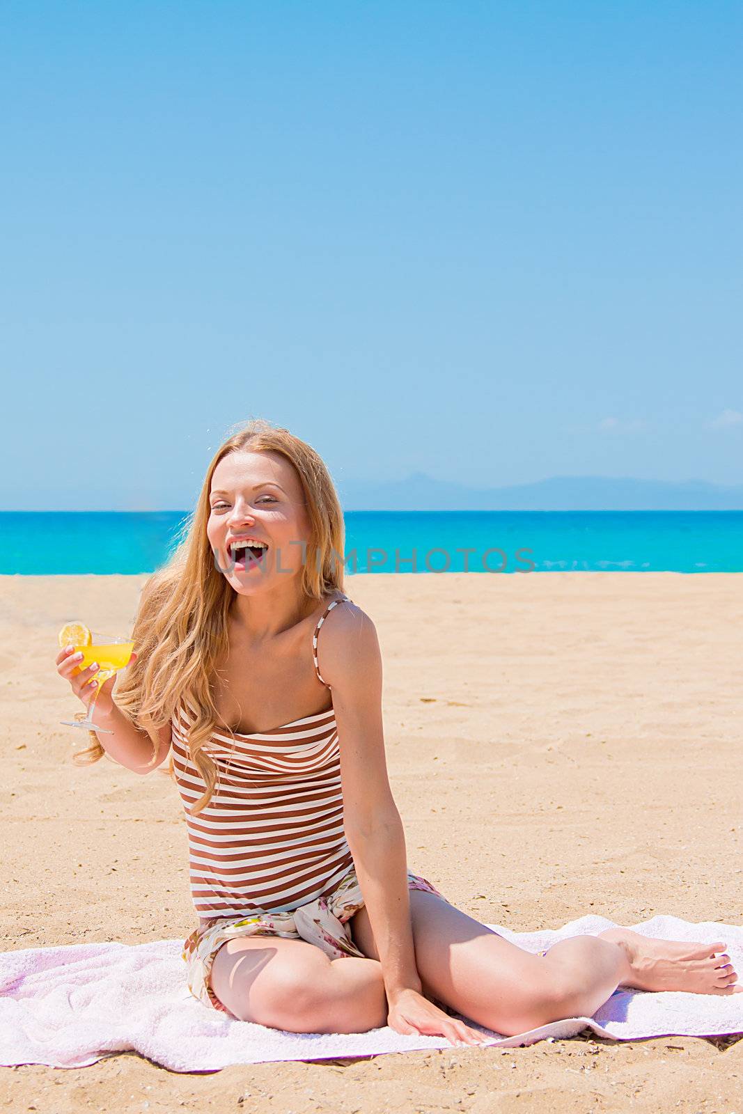 Photo of a young and beautiful woman who is resting on the beach and drink a drink from a glass
