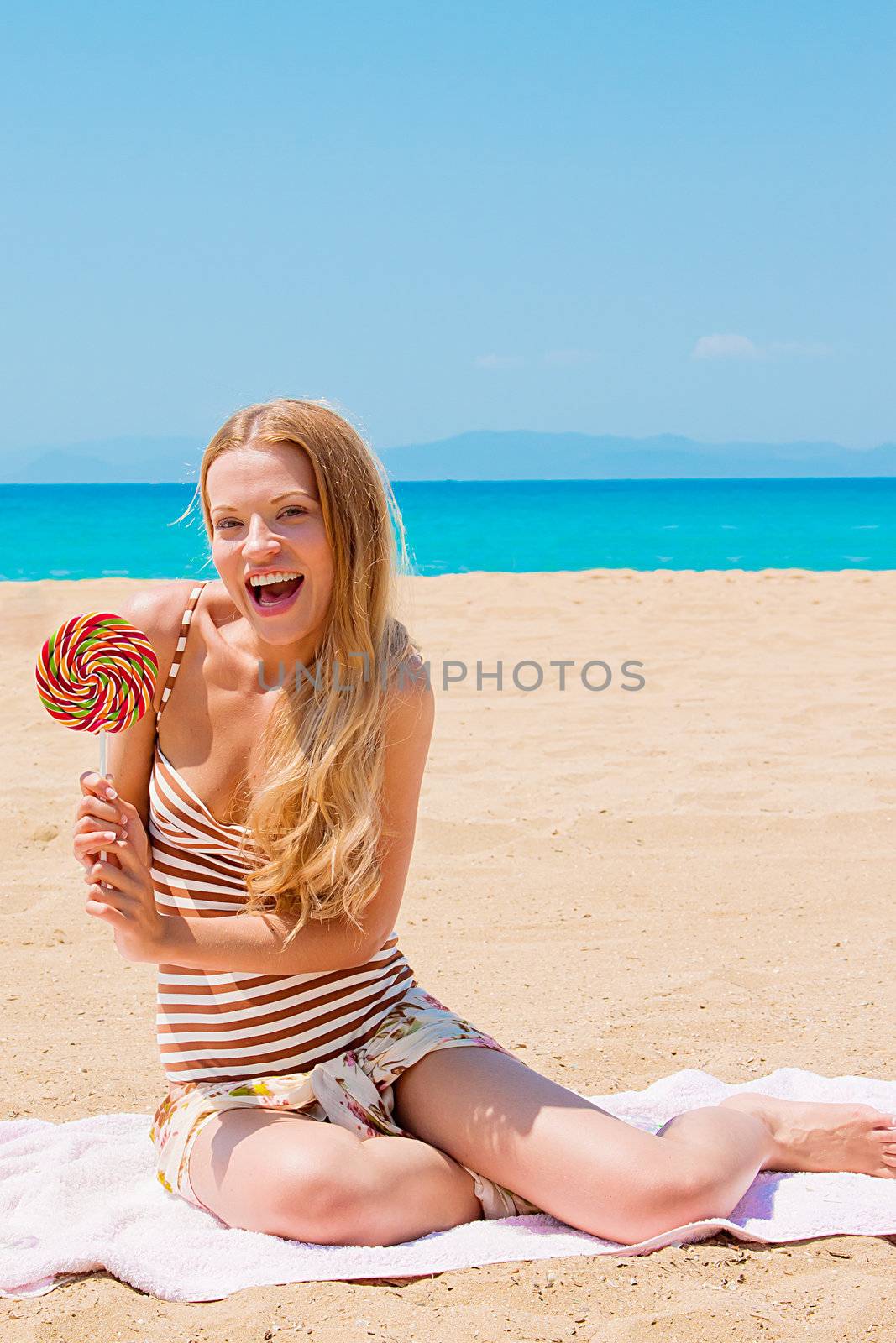 A young and beautiful woman with a lollipop resting on the beach