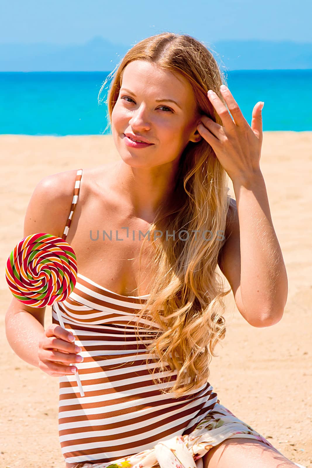 A young and beautiful woman with a lollipop resting on the beach