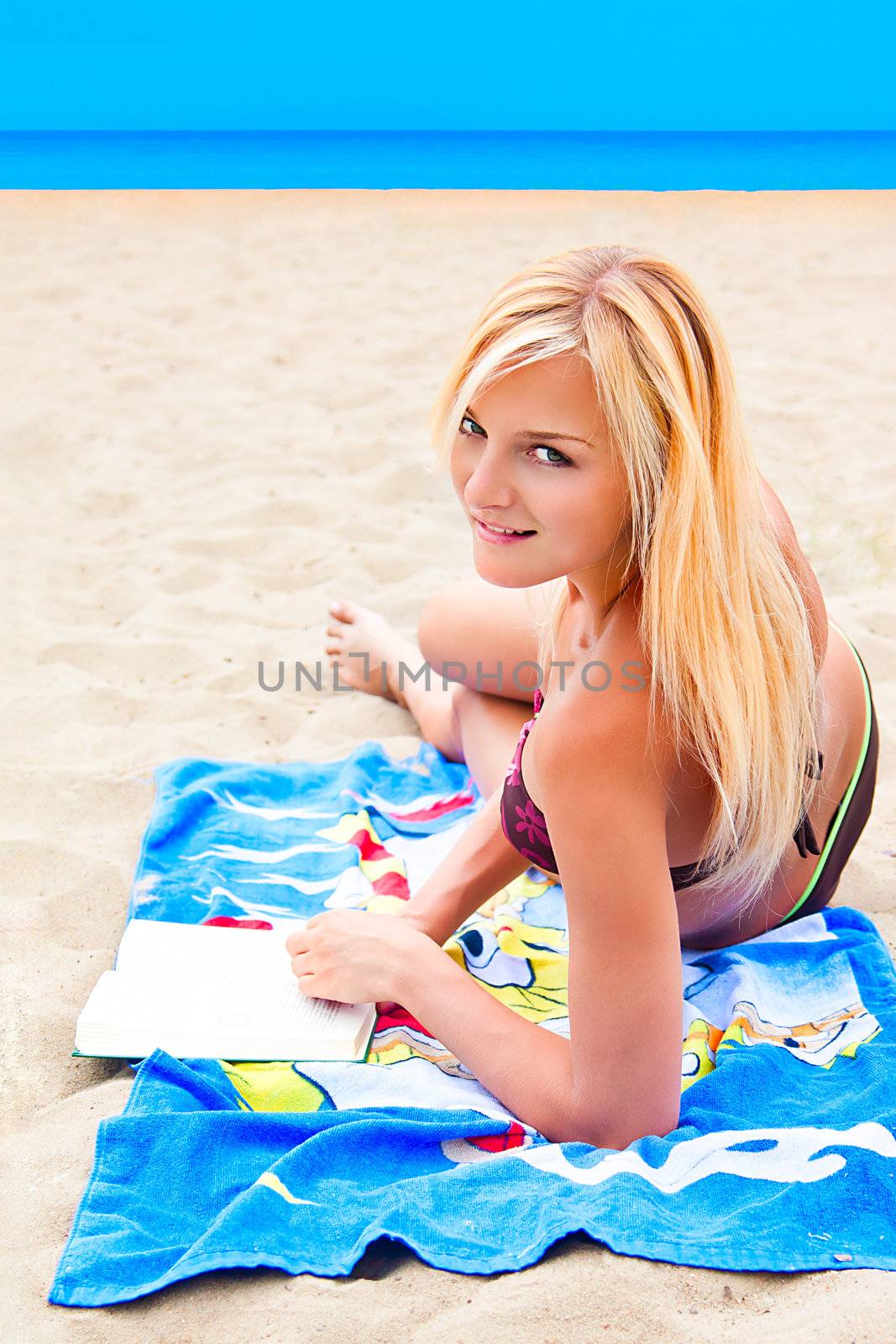 A young and beautiful woman resting on a beach reading a book in hard cover green