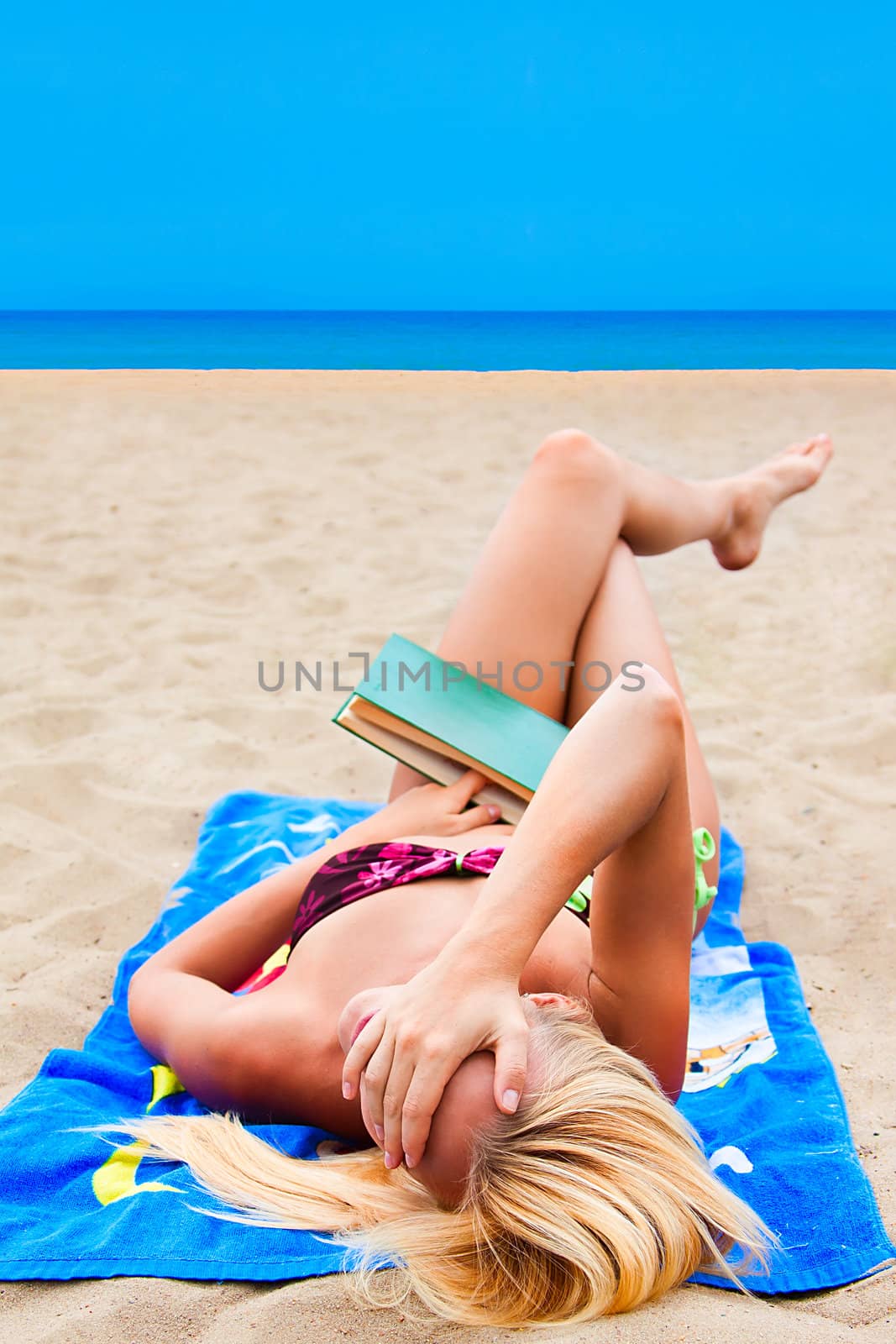 A young and beautiful woman resting on a beach reading a book in hard cover green