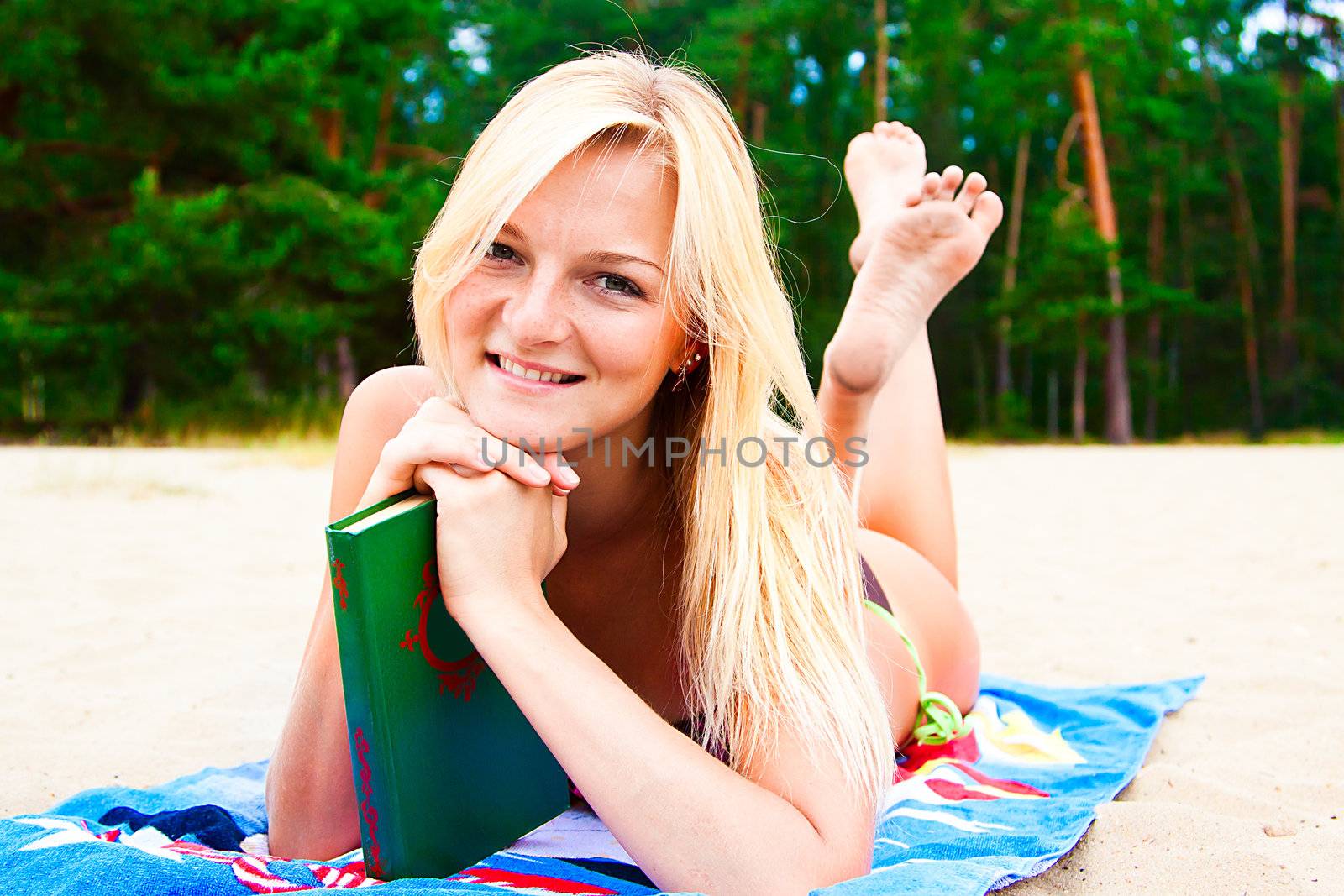 A young and beautiful woman resting on a beach reading a book in hard cover green