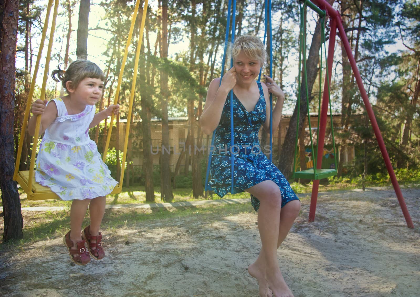 Mother and daughter on swing in summer park