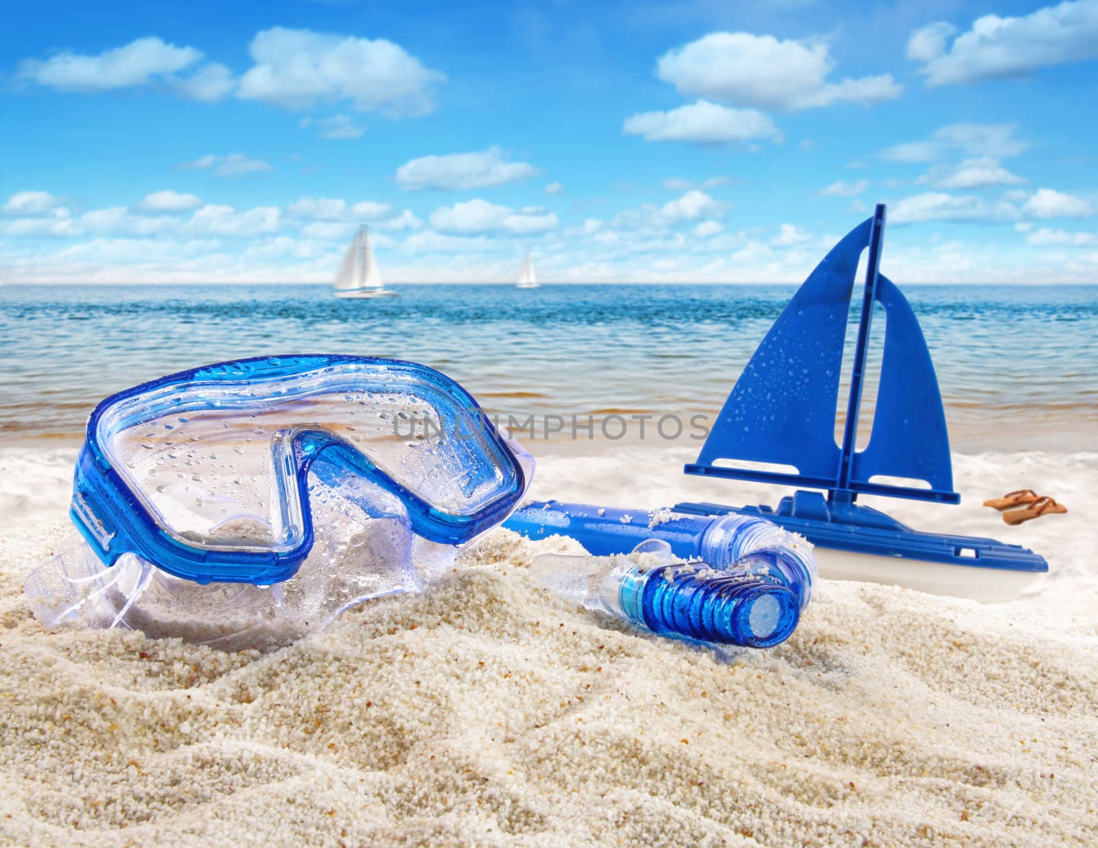 Goggles and toy sailboat in sand at the beach scene 