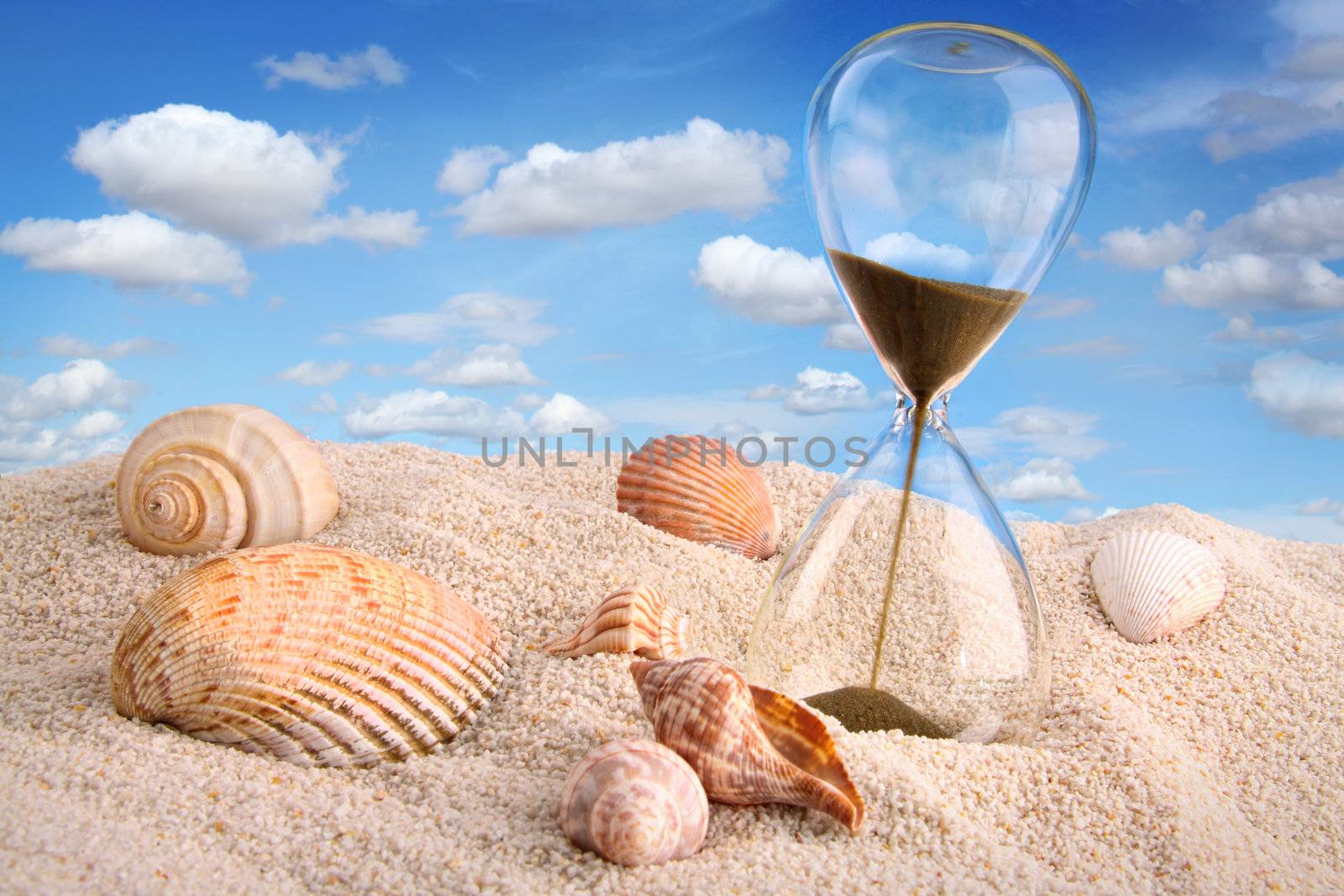 Hourglass in the sand with blue sky by Sandralise