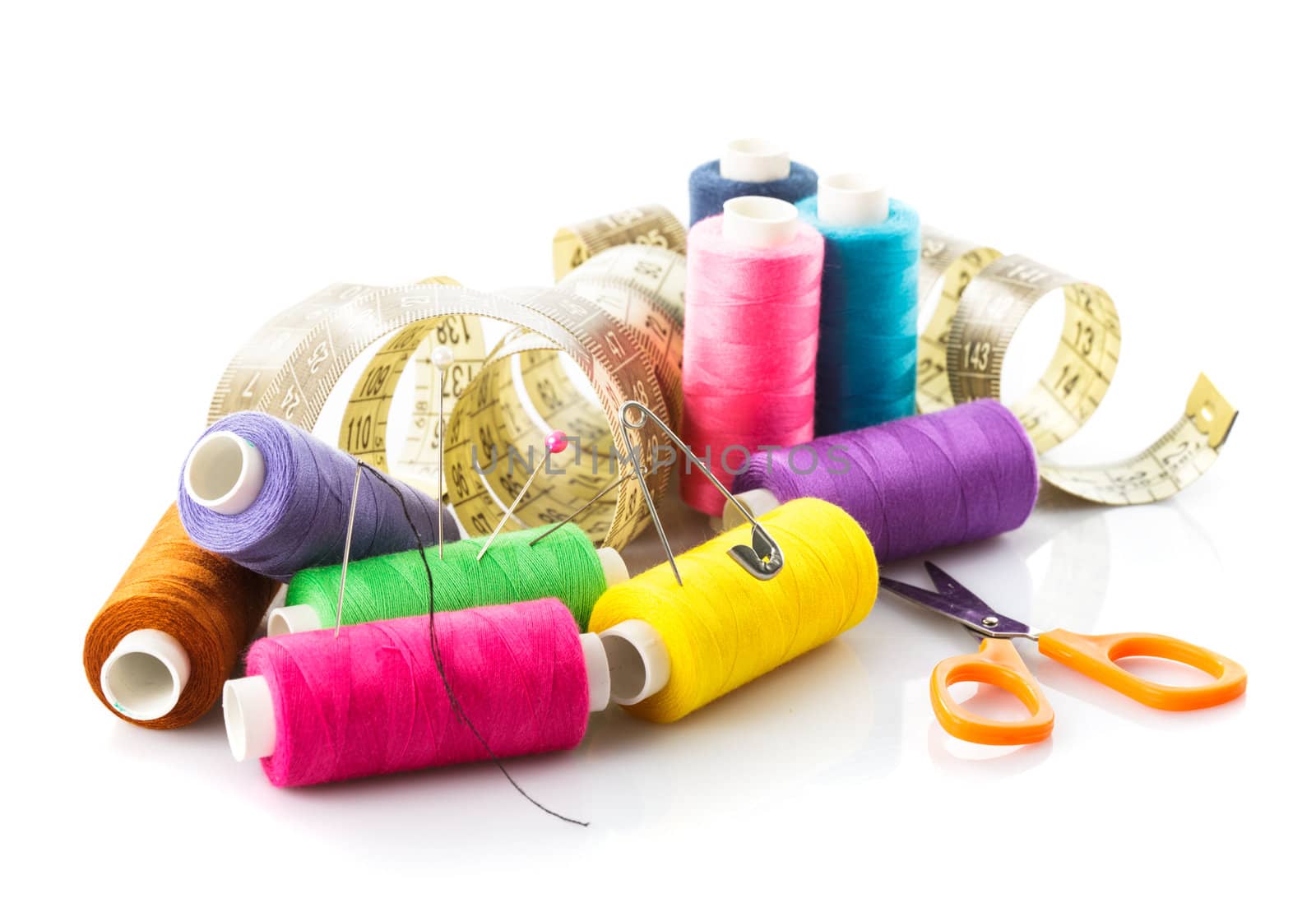 Sewing items: multicoloured threads, pins, meter and scissors on white