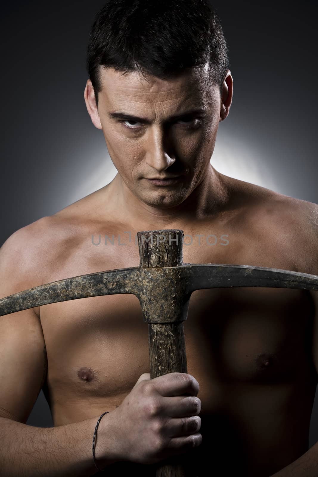 Topless construction worker with pick axe over grey background