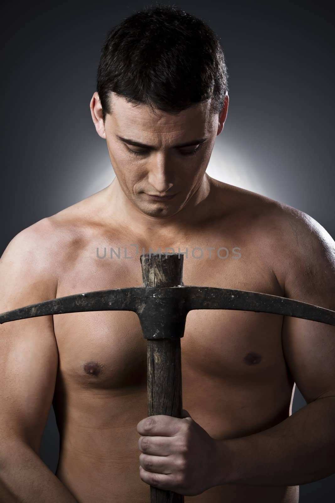 Topless construction worker with pick axe over grey background