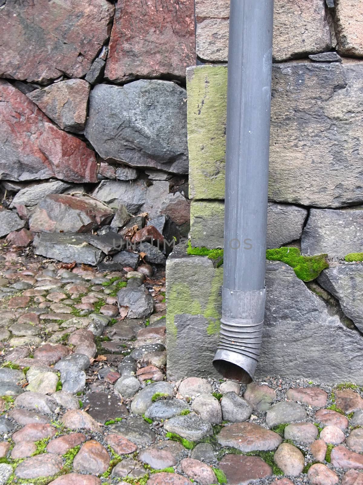 Drainpipe against old stone wall and pavement