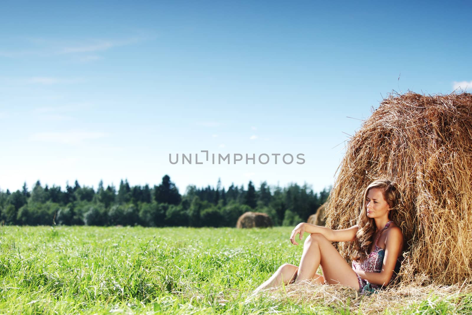 portrait of a girl next to a stack of hay under the blue sky