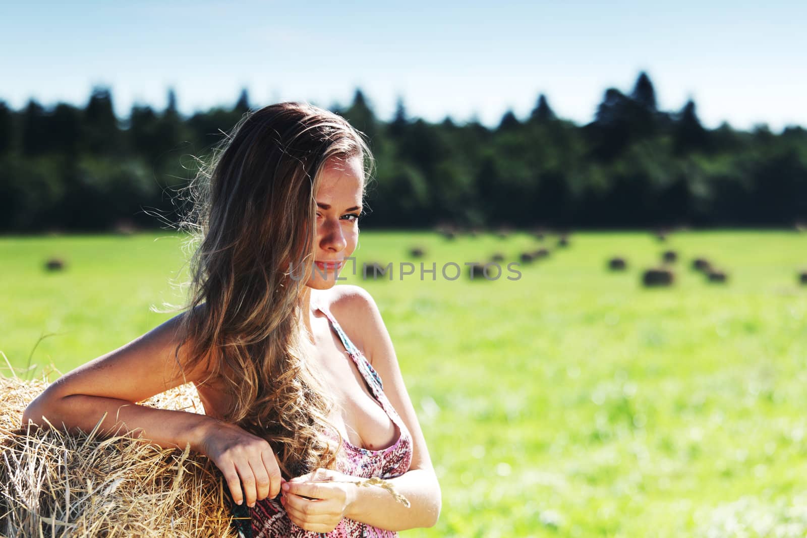 portrait of a girl next to a stack of hay under the blue sky