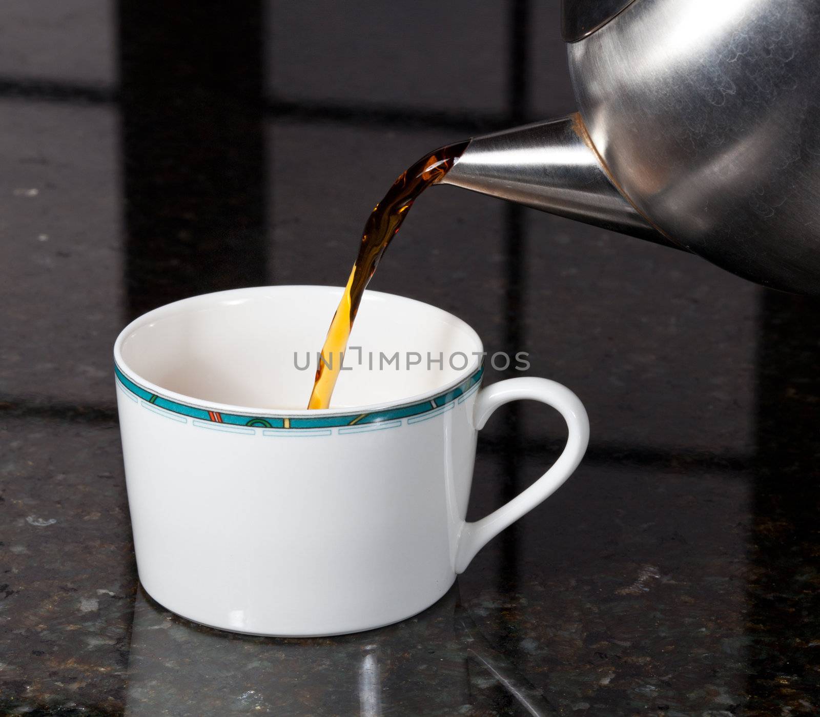 Fresh tea being poured into white cup on marble kitchen worktop