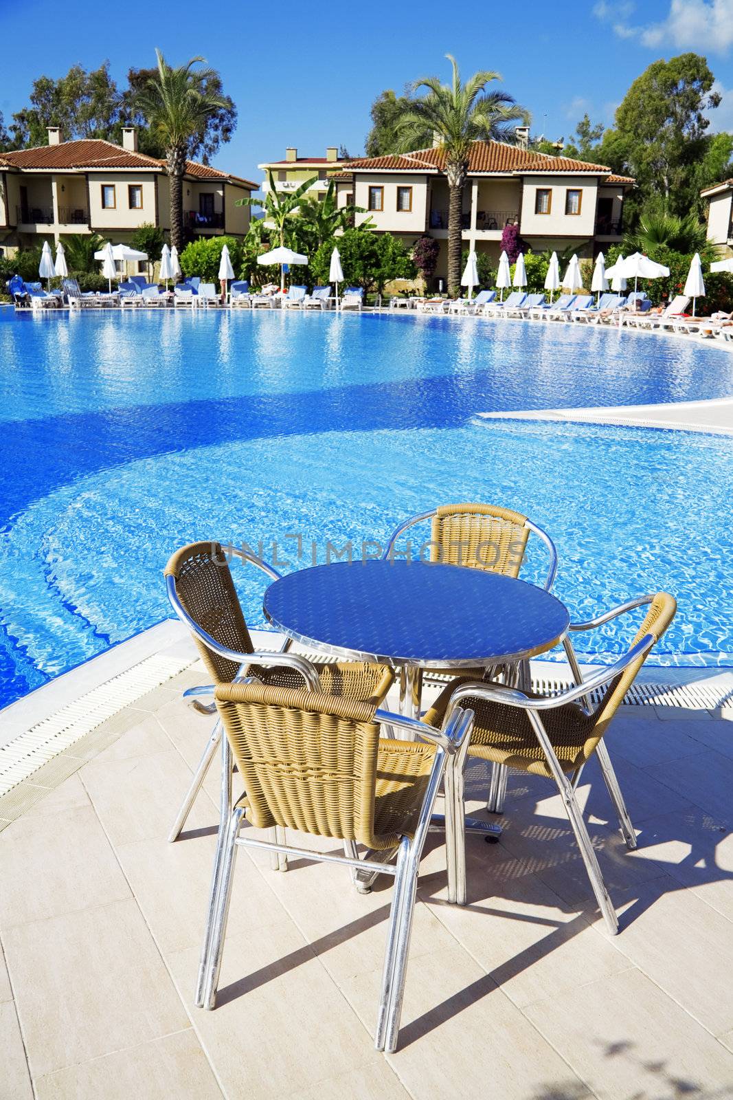 table and chairs near a cool pool in a hot canicular day by Serp