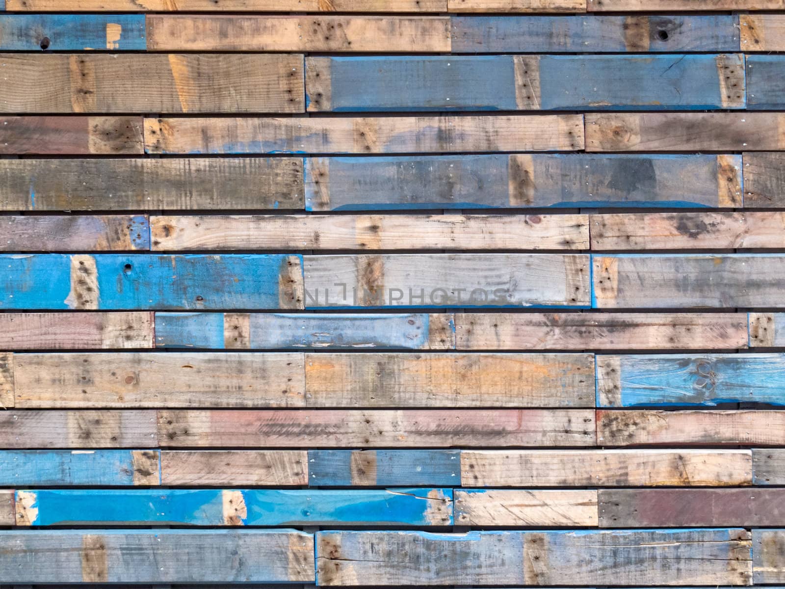 Background texture pattern of weathered wooden planks with grungy remnants of blue paint forming the siding of an exterior building wall