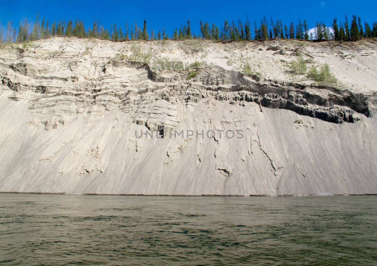 High cut bank of silt, sand and gravel slowly eroding by flowing water of mighty Yukon River, Yukon Territory, Canada