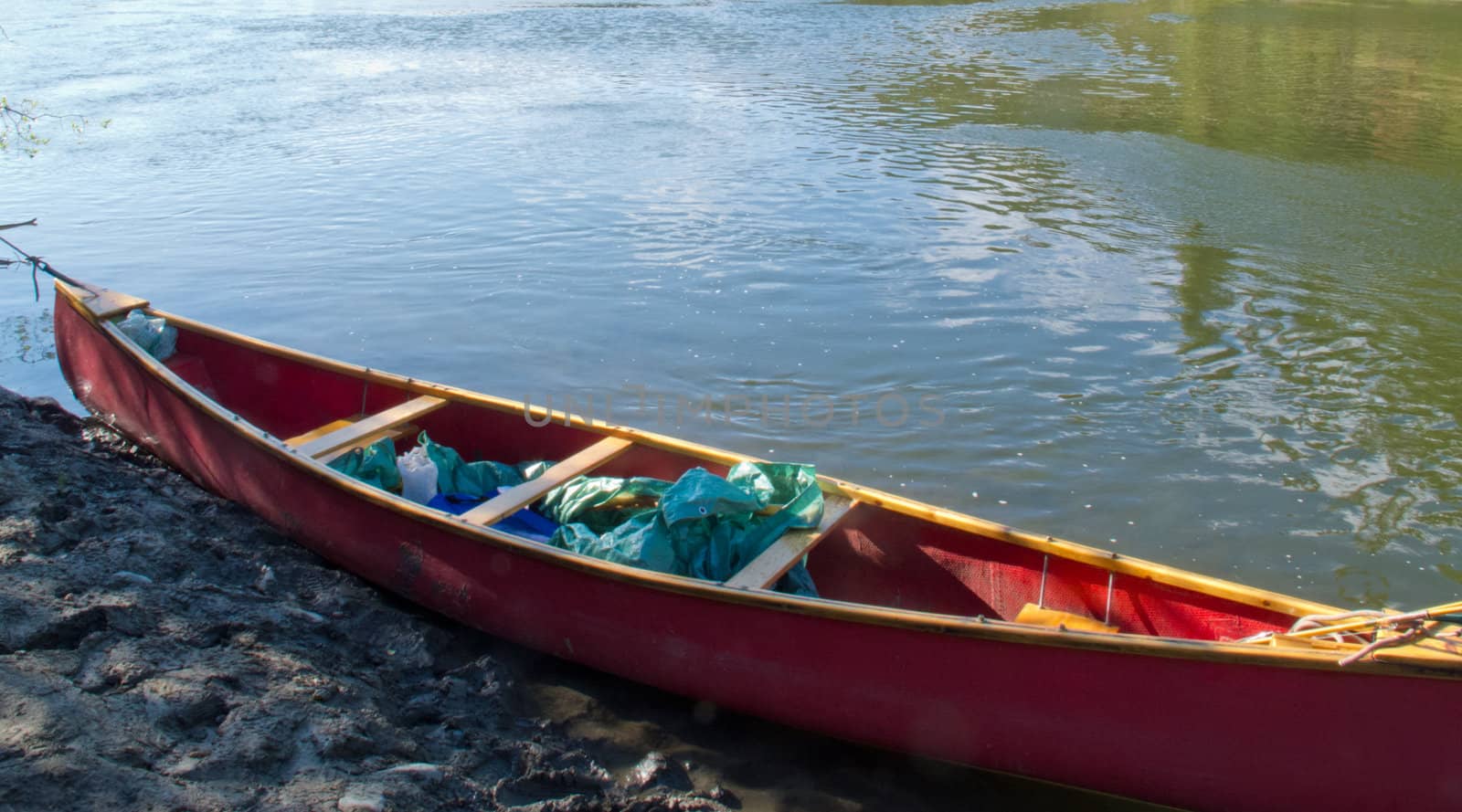 Red canoe at river shore the water of the river reflecting green hues of surrounding boreal forest wilderness