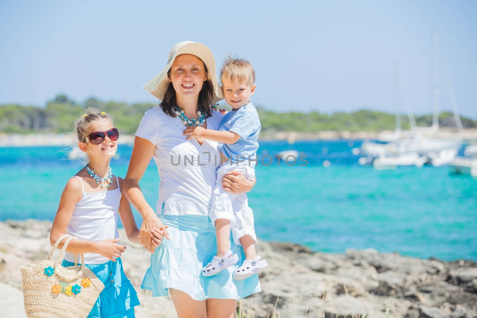 Family of three walking along tropical beach by maxoliki