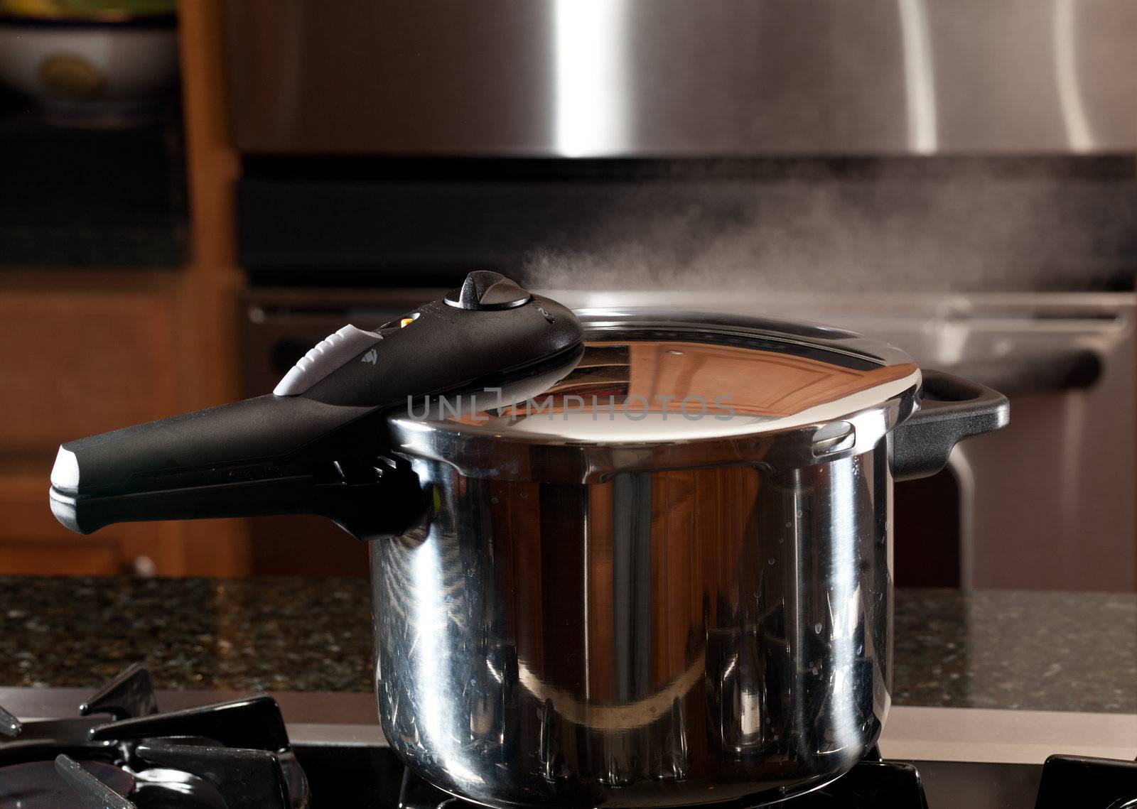 Steam escaping from lid of pressure cooker with reflection of modern kitchen
