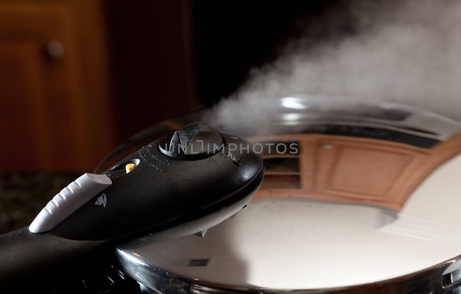 Steam escaping from lid of pressure cooker with reflection of modern kitchen