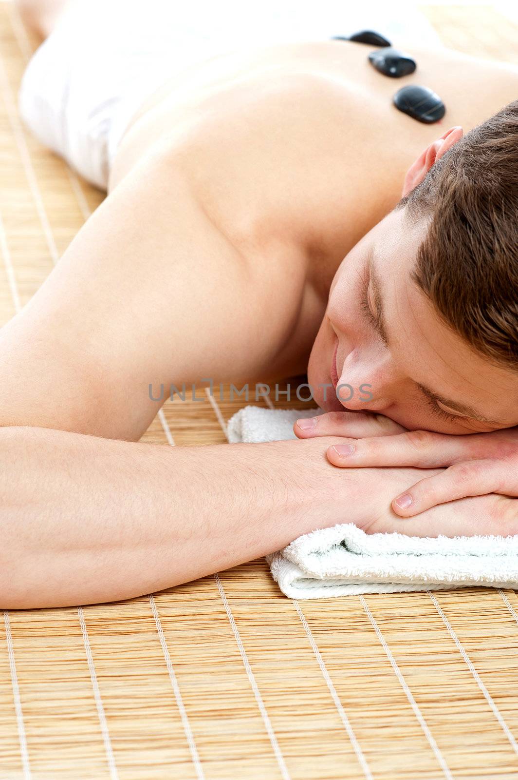 Man relaxing on carpet with hot stones. Cropped image