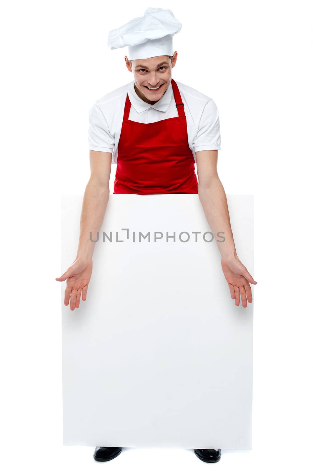 Handsome young cook showing blank billboard against white. Cheerful cook