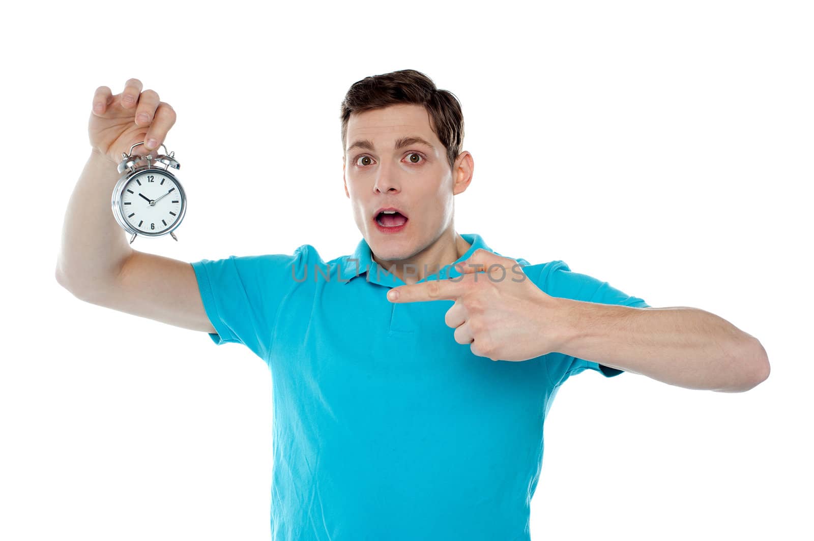 Shocked young guy holding alarm clock and pointing at it