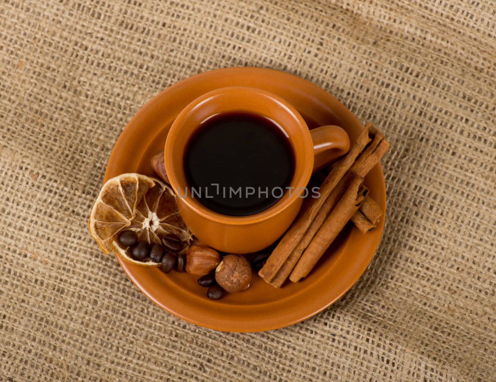 Closeup shot of freshly prepared cup of italian espresso with cinnamon, coffe beans, nuts and lemon over sacking
