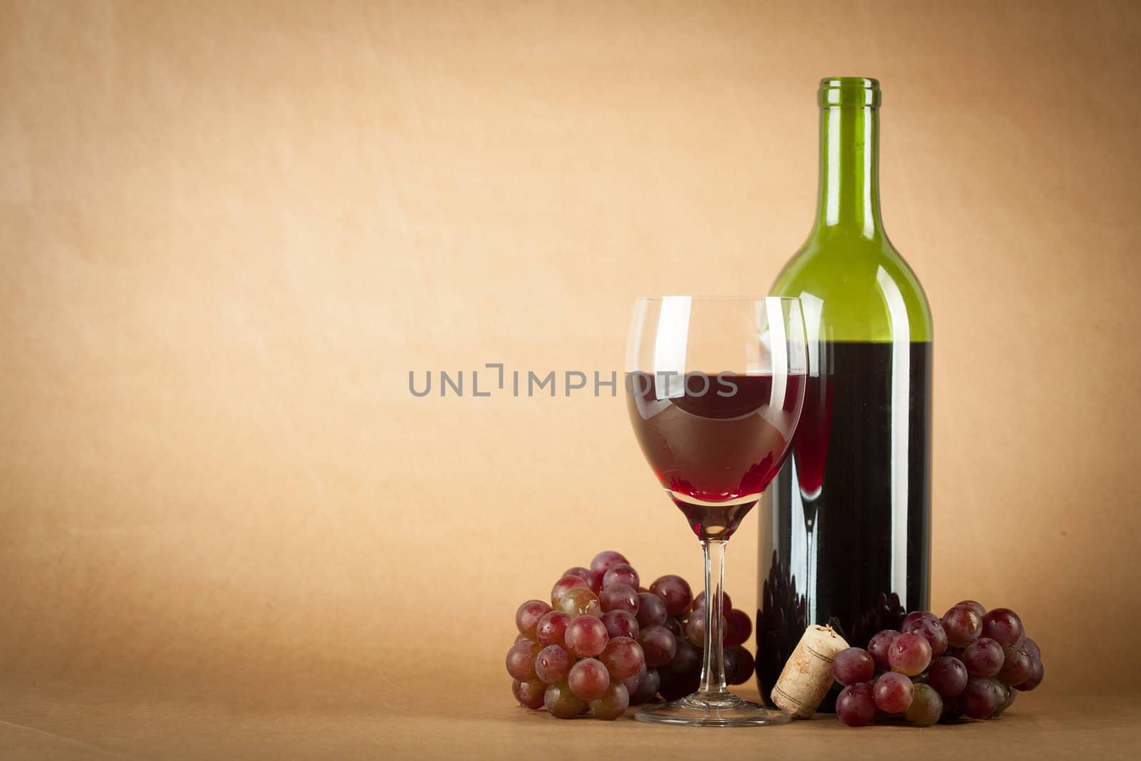 A bottle of red wine, a glass half full and grapes on a vintage orange background.