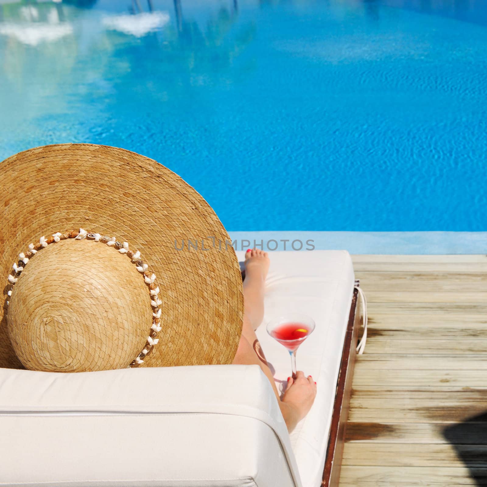 Woman in hat relaxing at the poolside with cosmopolitan cocktail