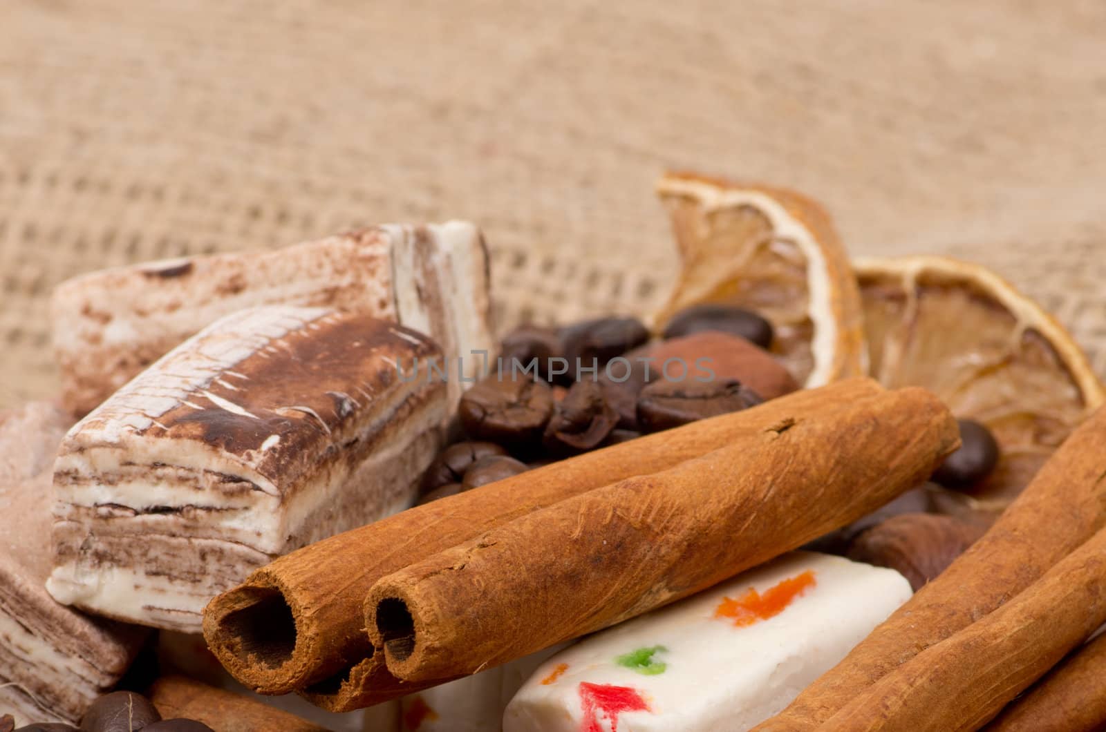 Sweets, cinnamon, nuts and coffee beans on a saucer, on burlap background.