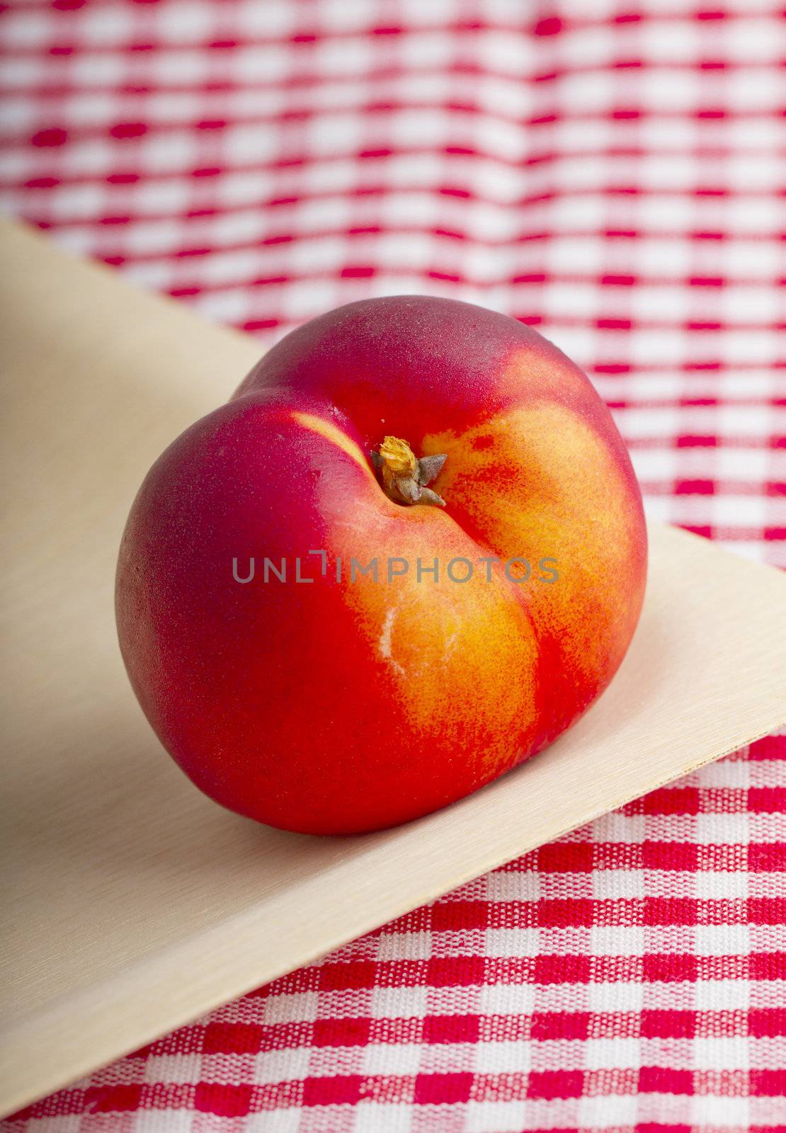 Single red peach over a wooden plate