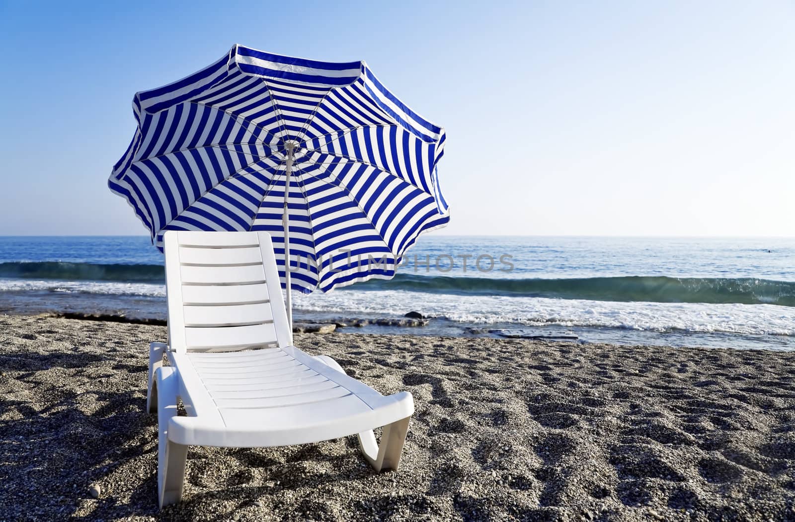 Chaise lounge with an umbrella standing alone on the bank of the blue sea by Serp