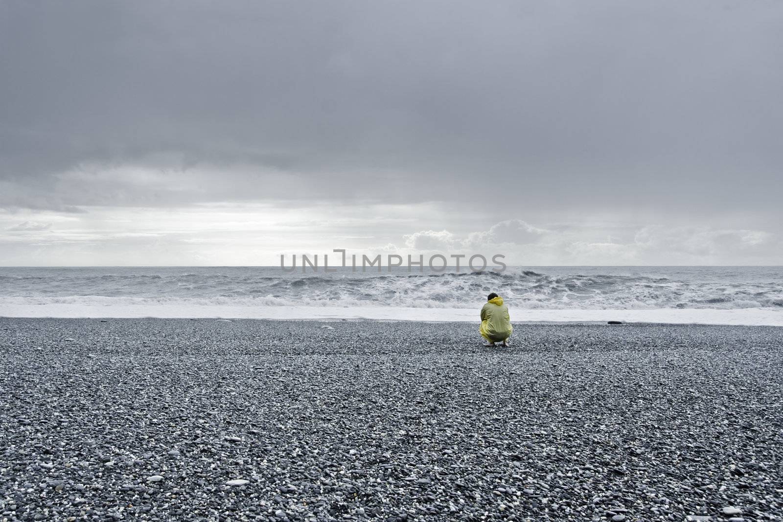 man in a yellow rain coat kneeling down at the ocean