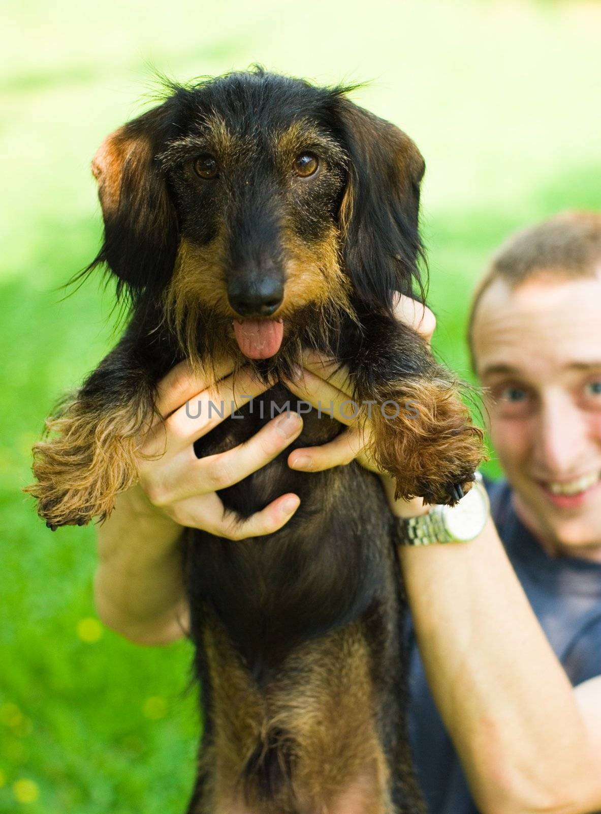 young man holding a dachshund up high into the camera