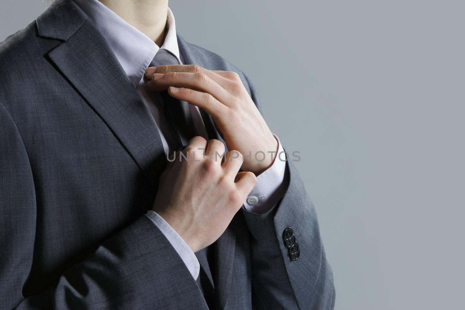 A businessman in a  grey suit checking his necktie
