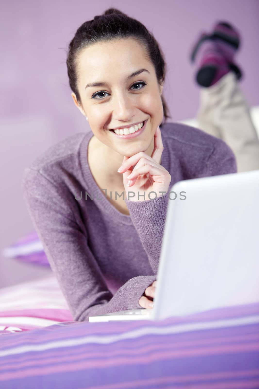 Portrait of a young female relaxing in bed while using laptop by stokkete