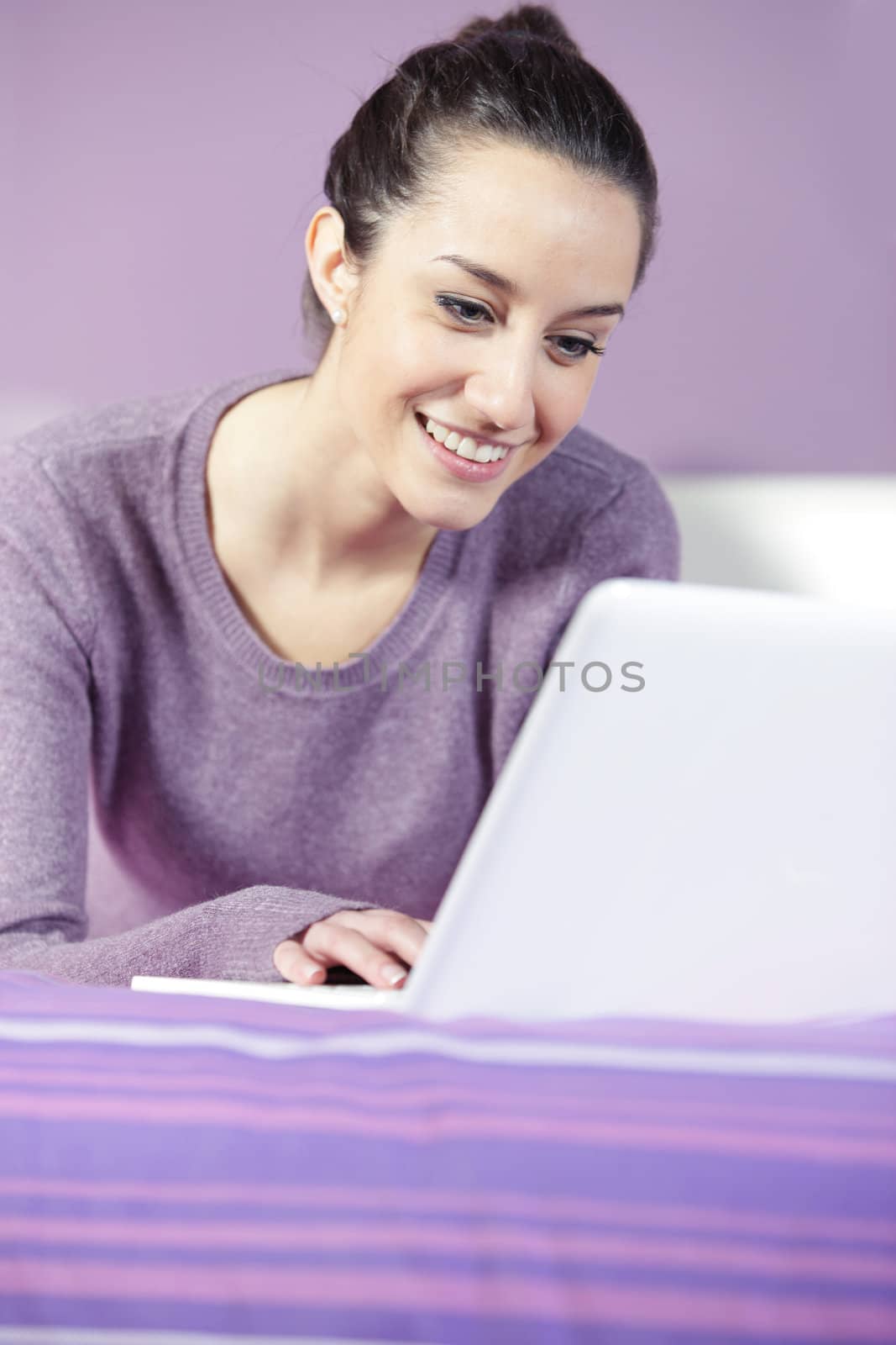 Portrait of a young female relaxing in bed while using laptop by stokkete