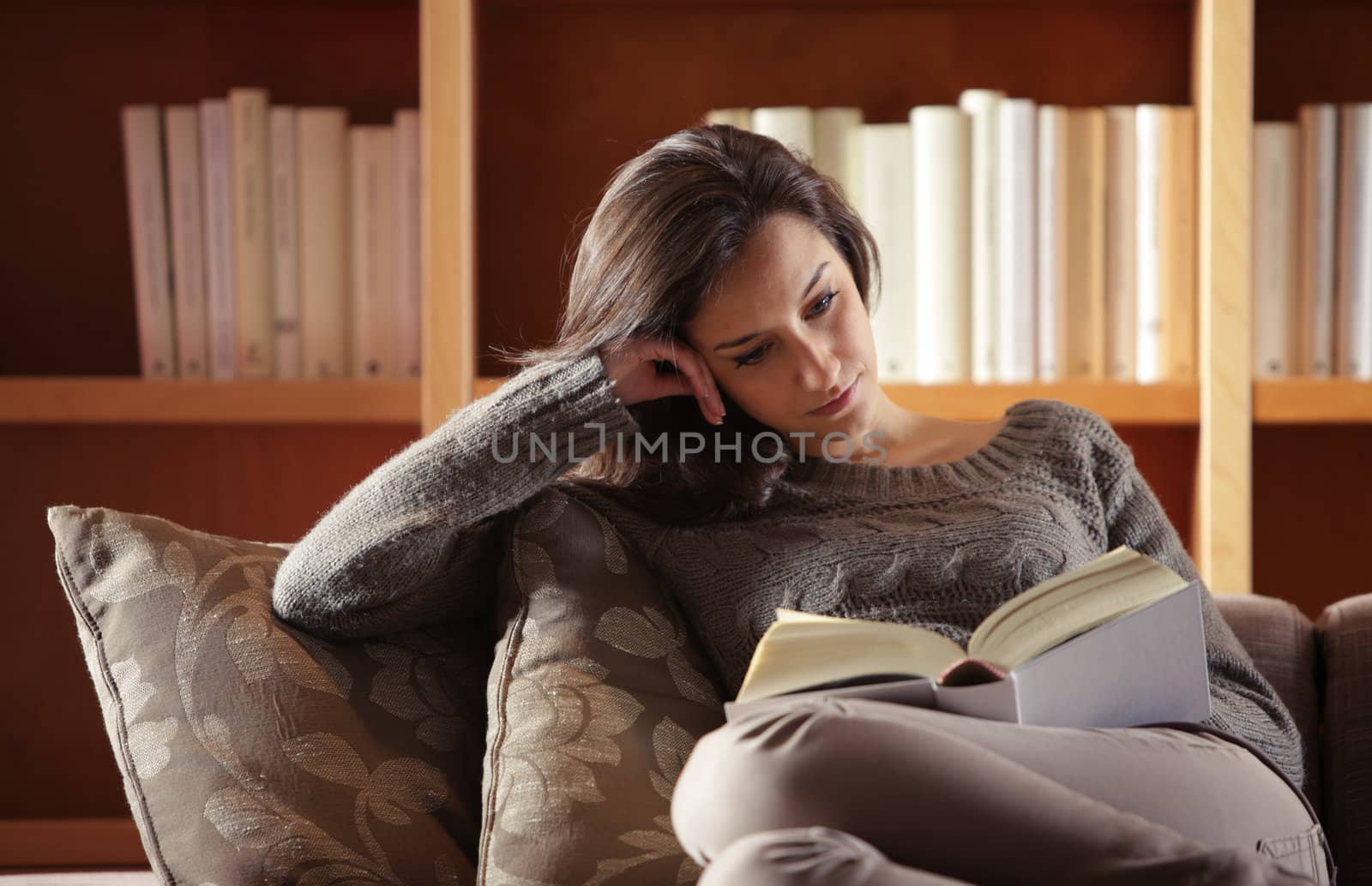 Portrait of a  young woman lying on couch with book by stokkete