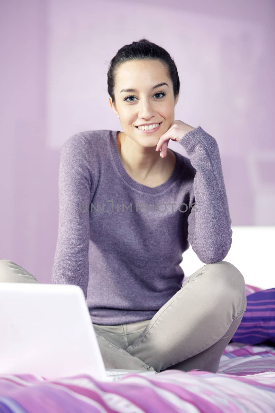 Portrait of a young female relaxing in bed while using laptop by stokkete