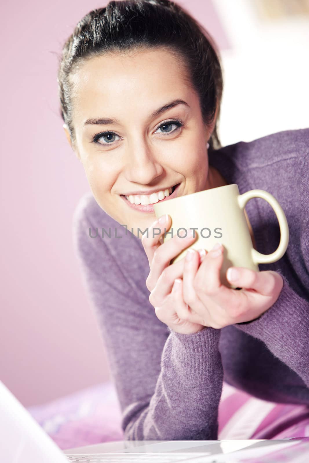 Portrait of a pretty happy young woman holding a cup of coffee in bed