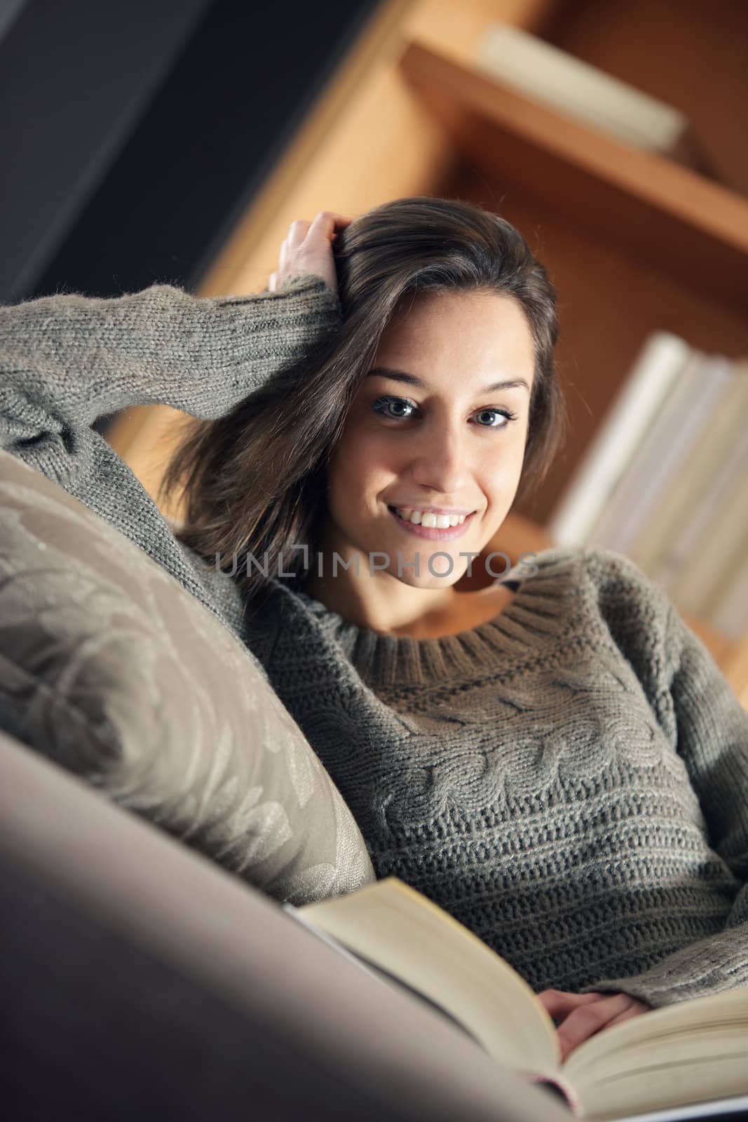 Portrait of a happy young woman lying on couch with book