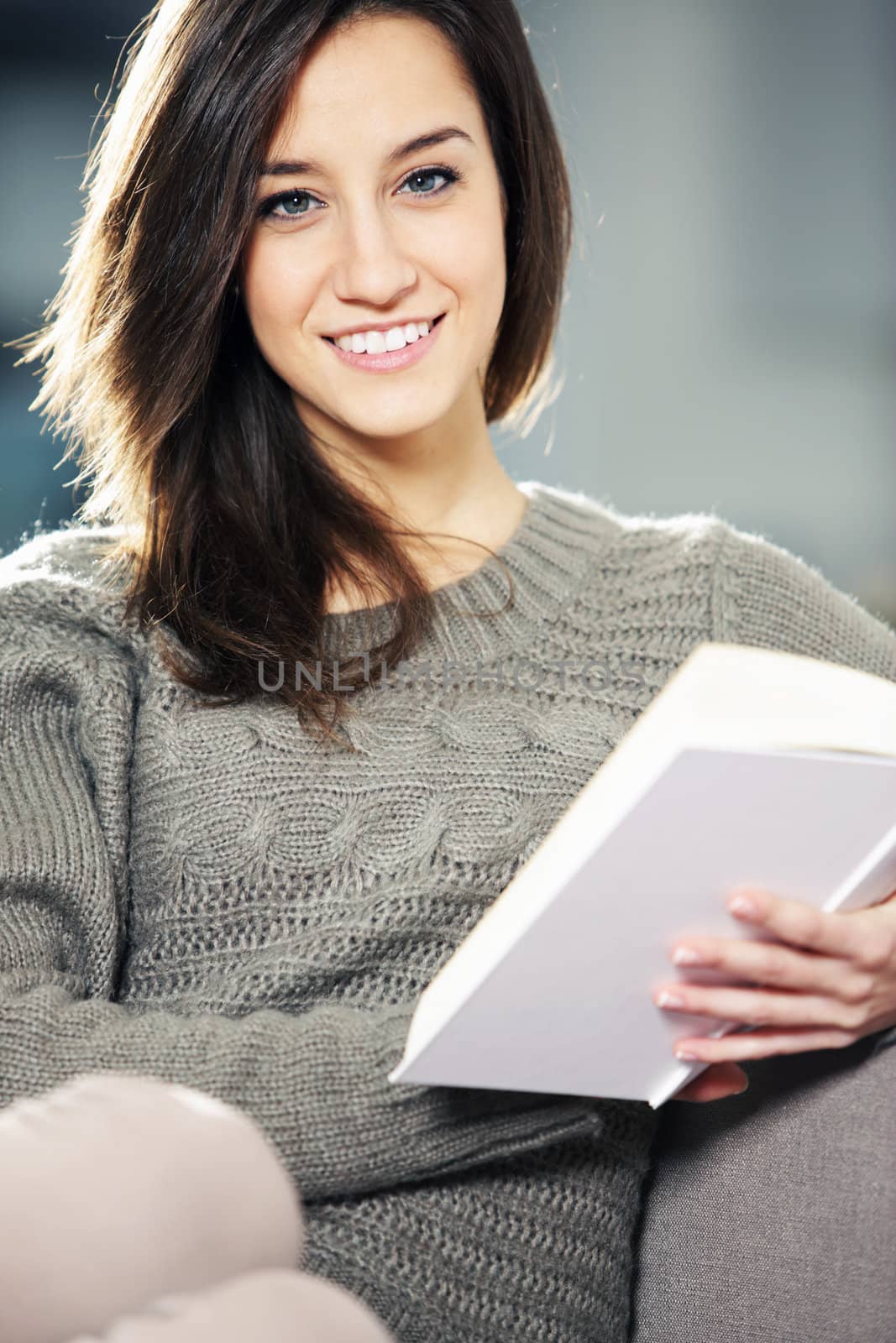 Portrait of a happy young woman lying on couch with book